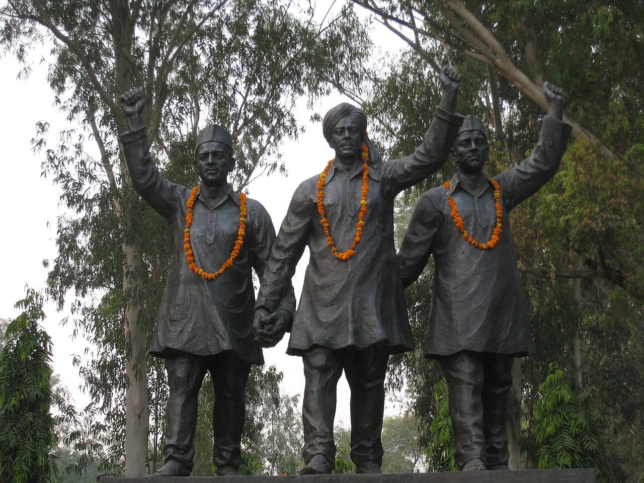 Garlanded bronze statues of Bhagat Singh, Rajguru and Sukhdev with raised fists among trees